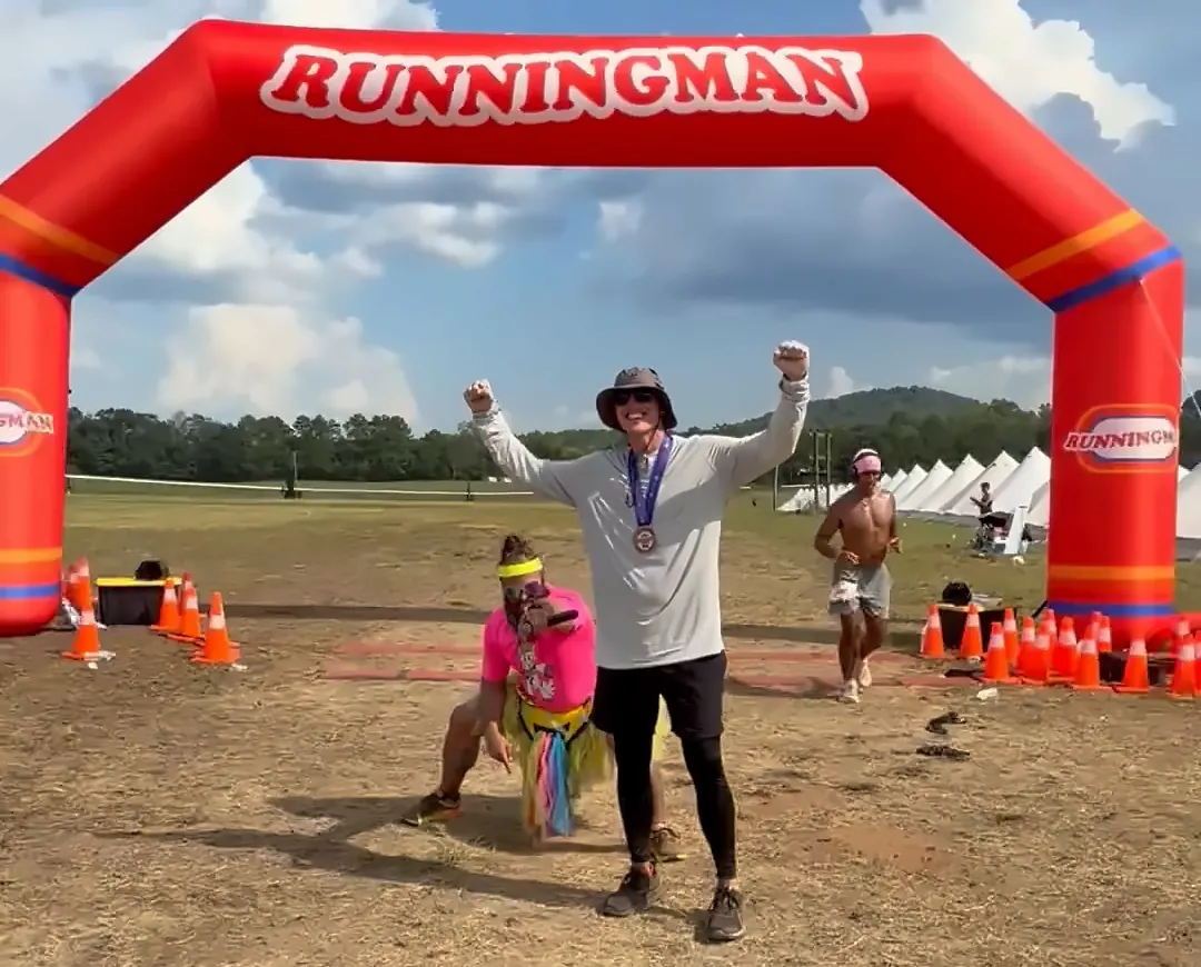 Brett Gillan with arms raised under the Runningman finish arch after his first marathon